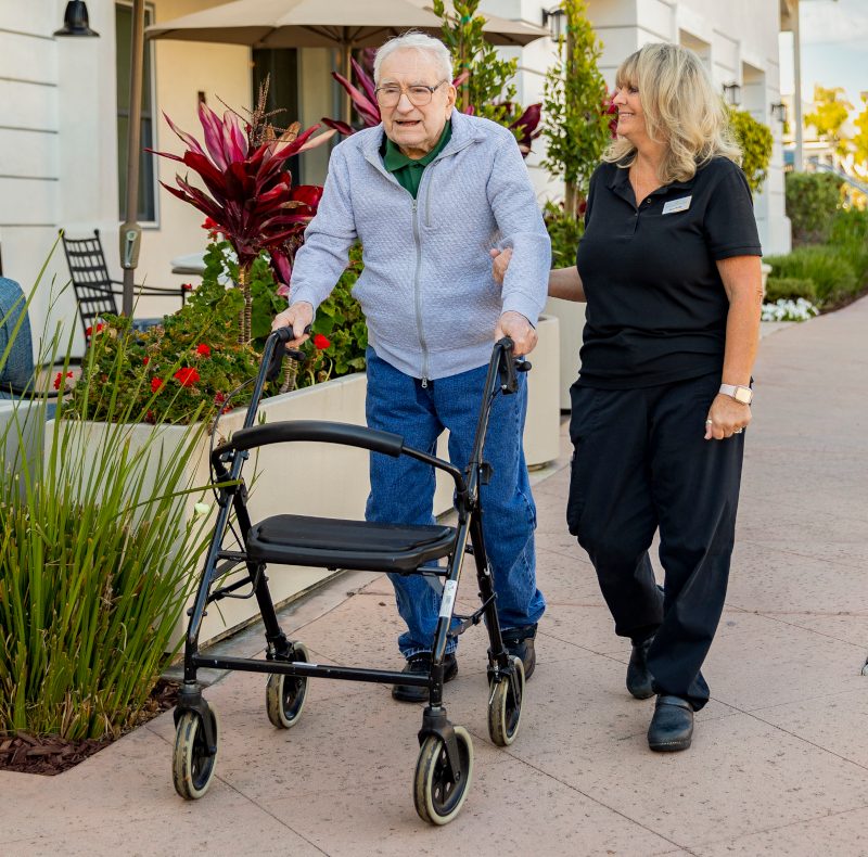 An elderly man on a walk with a care assistant.